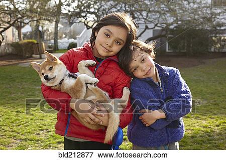 Stock Photo - Mixed race siblings holding puppy in backyard. Fotosearch