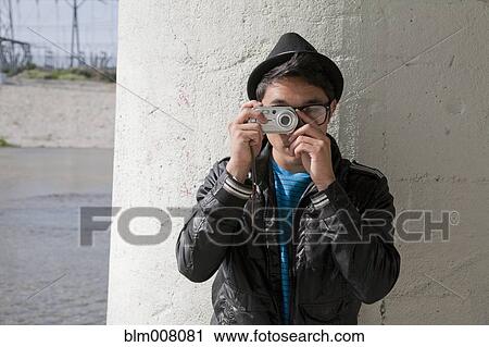 Stock Image - Mixed race teenage boy taking photograph with digital camera. Fotosearch