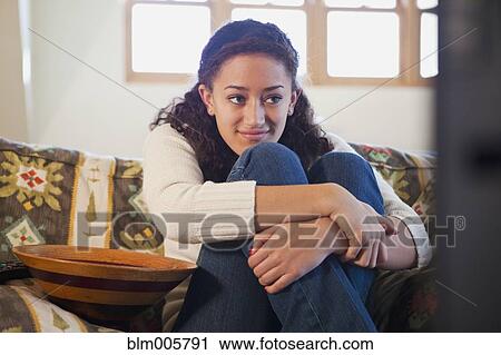 Stock Image - Mixed race teenager sitting on sofa in living room. Fotosearch
