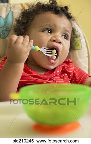 Stock Photography - Mixed race toddler boy eating in high chair. Fotosearch