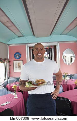Stock Photo - Mixed race waiter holding plate of food in restaurant. Fotosearch