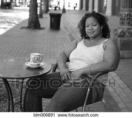 Stock Image - Mixed race woman drinking coffee at sidewalk cafe. Fotosearch