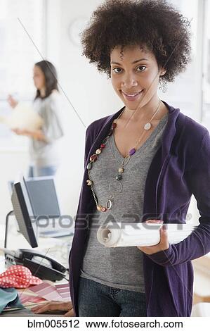 Stock Image - Mixed race woman holding blueprints in office. Fotosearch