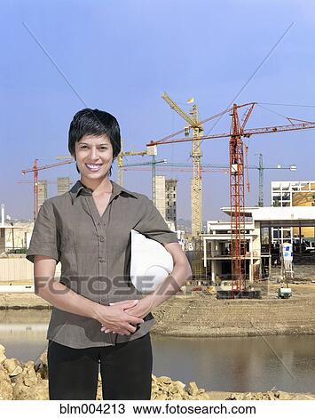 Mixed race woman holding hard-hat with construction site in background View Large Photo Image Stock Image - Mixed race woman holding hard-hat with construction site in background. Fotosearch
