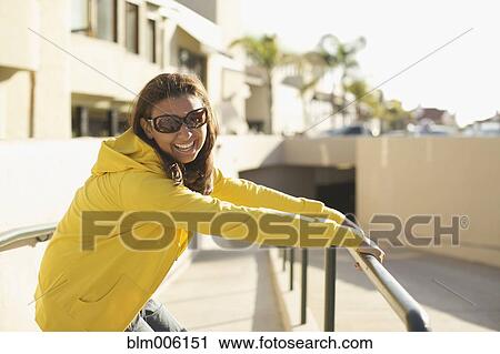 Stock Image - Mixed race woman in sunglasses leaning on railing. Fotosearch