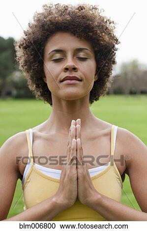 Stock Image - Mixed race woman practicing yoga in park. Fotosearch