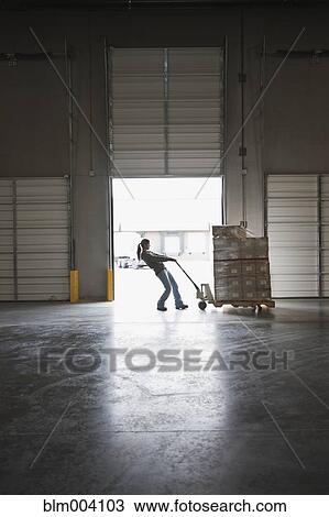 Stock Image - Mixed race woman pulling boxes on pallet in warehouse. Fotosearch