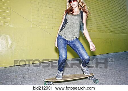 Stock Image - Mixed race woman riding skateboard on city street. Fotosearch
