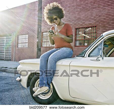 Stock Photo - Mixed race woman sitting on vintage car. Fotosearch