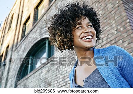 Mixed race woman smiling below urban building View Large Photo Image Stock Photograph - Mixed race woman smiling below urban building. Fotosearch