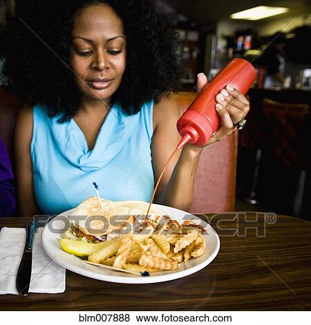 Mixed race woman squeezing ketchup on french fries in diner booth View Large Photo Image Stock Photo - Mixed race woman squeezing ketchup on french fries in diner booth. Fotosearch