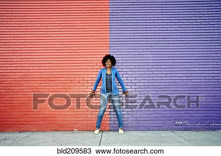 Stock Image - Mixed race woman standing by colorful wall. Fotosearch