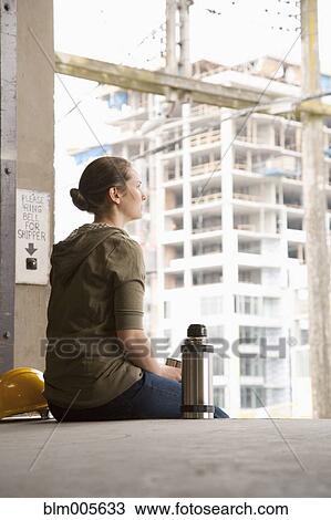 Stock Image - Mixed race woman taking a break on warehouse loading dock. Fotosearch