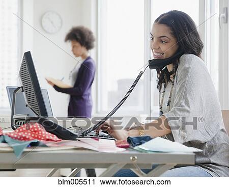Stock Image - Mixed race woman talking on telephone in office. Fotosearch