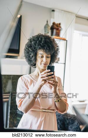 Stock Image - Mixed race woman using cell phone in living room. Fotosearch