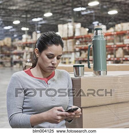 Stock Photography - Mixed race woman using cell phone in warehouse. Fotosearch