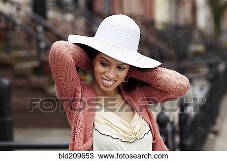 Stock Image - Mixed race woman wearing hat on city street. Fotosearch