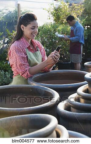 Stock Photo - Mixed race woman working in garden nursery checking cell phone. Fotosearch