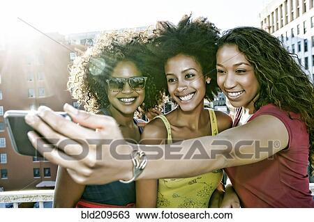 Stock Image - Mixed race women taking self-portrait on urban rooftop. Fotosearch