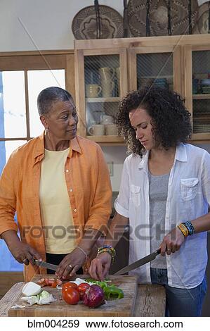 Stock Photo - Mother and daughter cutting vegetables in kitchen. Fotosearch