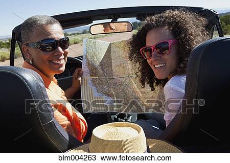 Stock Image - Mother and daughter holding map in convertible. Fotosearch