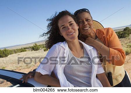 Stock Photography - Mother and daughter hugging against convertible. Fotosearch