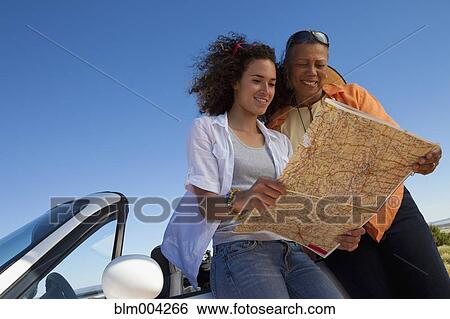 Mother and daughter leaning against convertible and looking at map View Large Photo Image Stock Photograph - Mother and daughter leaning against convertible and looking at map. Fotosearch