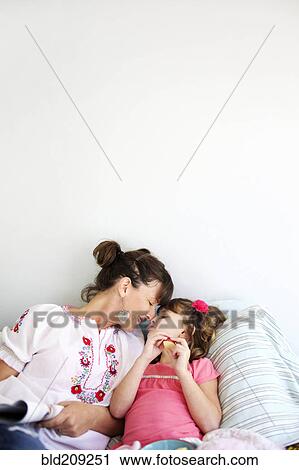 Stock Image - Mother and daughter relaxing on bed. Fotosearch