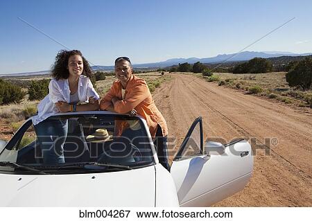 Stock Photo - Mother and daughter standing in convertible on dirt road. Fotosearch
