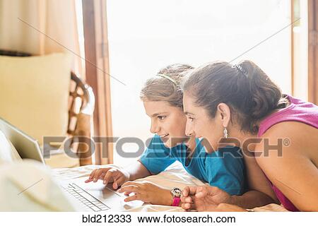 Stock Image - Mother and daughter using laptop at desk. Fotosearch
