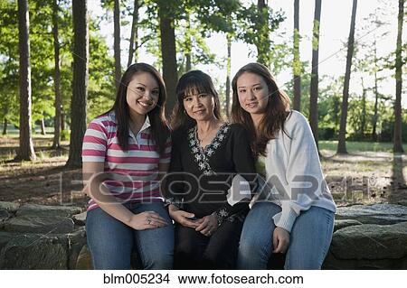 Picture - Mother and mixed race daughters sitting on stone wall. Fotosearch
