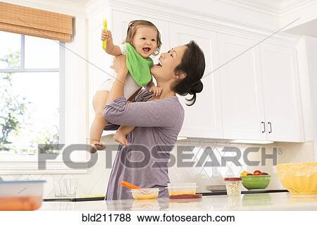 Mother holding baby girl in kitchen View Large Photo Image Stock Photo - Mother holding baby girl in kitchen. Fotosearch