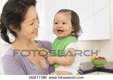 Mother holding baby girl in kitchen View Large Photo Image Stock Photograph - Mother holding baby girl in kitchen. Fotosearch