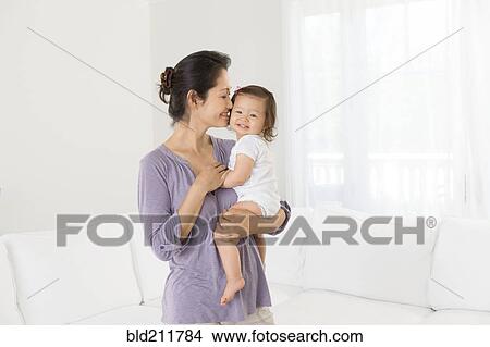 Picture - Mother holding baby girl in living room. Fotosearch