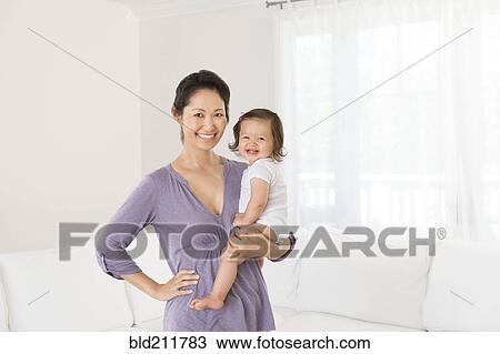 Stock Image - Mother holding baby girl in living room. Fotosearch