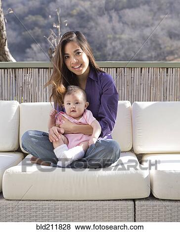 Stock Photo - Mother holding baby girl on patio sofa. Fotosearch