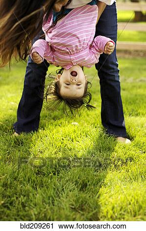 Stock Image - Mother holding toddler daughter upside down. Fotosearch