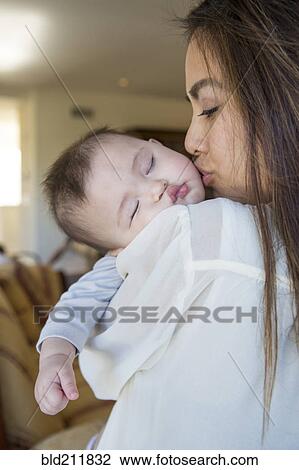 Stock Image - Mother kissing sleeping baby girl. Fotosearch