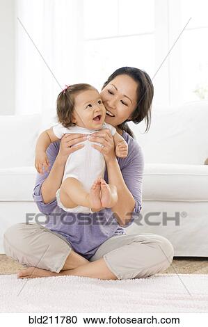 Stock Image - Mother playing with baby girl in living room. Fotosearch
