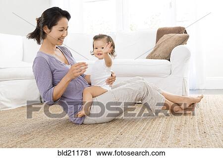 Stock Image - Mother playing with baby girl in living room. Fotosearch