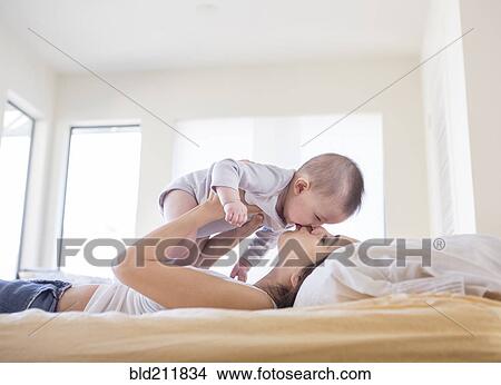 Picture - Mother playing with baby girl on bed. Fotosearch