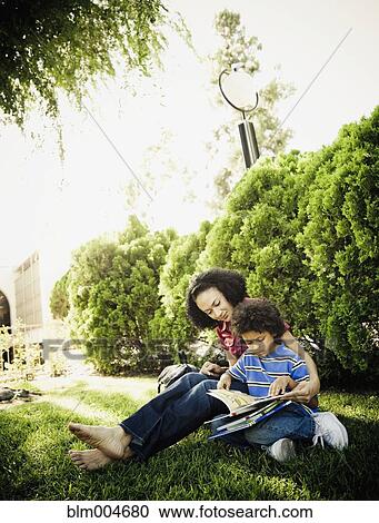 Stock Image - Mother reading books with son in park. Fotosearch