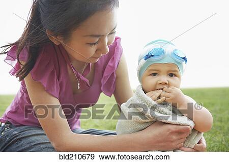 Stock Photo - Mother wrapping baby in towel outdoors. Fotosearch