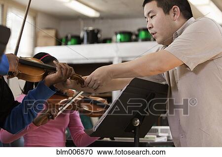Stock Image - Music teacher helping students in high school orchestra. Fotosearch