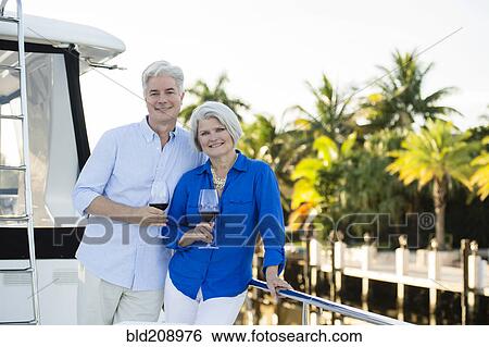 Stock Photograph - Older Caucasian couple having wine on boat deck. Fotosearch