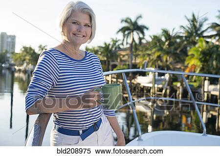 Stock Photography - Older Caucasian woman having coffee on boat deck. Fotosearch