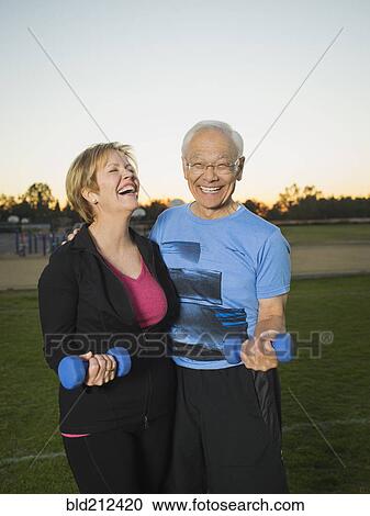 Stock Image - Older couple lifting weights together in urban park. Fotosearch