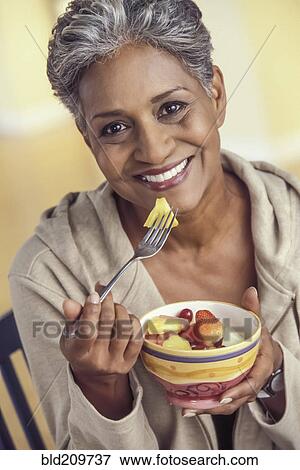 Stock Photo - Older woman eating bowl of fruit. Fotosearch