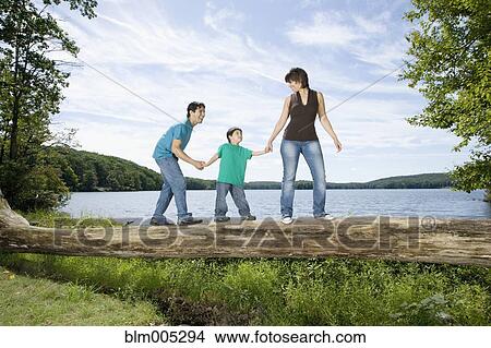 Picture - Parents helping son walk across log. Fotosearch