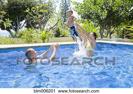 Stock Image - Parents throwing son in swimming pool. Fotosearch